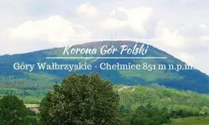 Widok na górzysty krajobraz z dominującym szczytem Chełmiec. Na pierwszym planie bujna zieleń drzew, w tle łagodne zbocza Gór Wałbrzyskich.