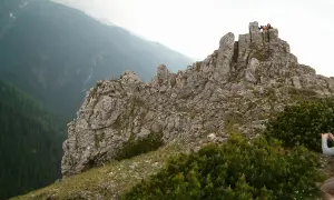 Sarnia skała wznosi się dumnie, otoczona zielenią. Na szczycie widać ludzi podziwiających panoramę.