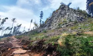 Kamienista ścieżka prowadzi ku skalnej grani z platformą widokową. To szlak na Trojak w Lądku-Zdroju, otoczony dziką przyrodą.