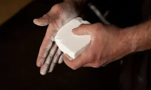 Dłonie pokryte białą substancją, trzymają kostkę magnezji. To właśnie magnezja co to jest, pomaga w pewnym chwycie.