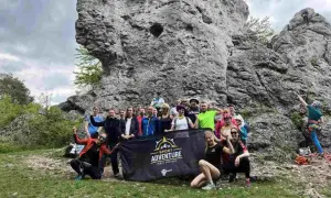 Grupa entuzjastów wspinaczki na Jurze Krakowsko-Częstochowskiej pozuje do zdjęcia z banerem "Sport Adventure".