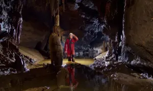 Eksplorator w czerwonym kombinezonie w jaskini z wodą. To jest właśnie speleologia co to – badanie podziemnych światów.