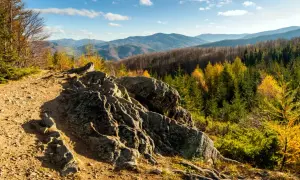 Szlak górski z kamienistą ścieżką i skalnym usypiskiem. W tle jesienny las i pasmo górskie.