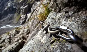 Stalowa lina i karabińczyk na skale, element ułatwiający wspinaczkę na via ferrata Czechy. Widok na zbocze.