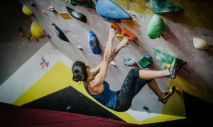 Kobieta wspina się po kolorowej ścianie, chwytając się pomarańczowych uchwytów. To właśnie bouldering – sportowa wspinaczka bez lin.