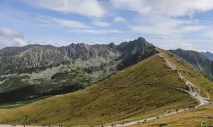 Tłum turystów wędruje kamienistym szlakiem na Kasprowy Wierch. Widok na skaliste szczyty Tatr i zielone doliny.