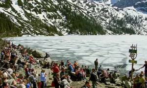Tłum ludzi odpoczywa nad zamarzniętym jeziorem Morskie Oko, w tle góry pokryte śniegiem i lasem. Palenica Białczańska w oddali.