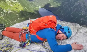 Zmęczony wspinacz odpoczywa na skale po wejściu na mnicha. Widok na jezioro i góry.