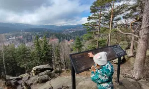 Dziecko w czapce z uszami poznaje mapę szlaków w Karpaczu. Widok na góry i miasto.