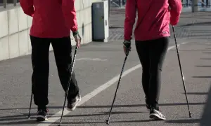 Dwie osoby w czerwonych kurtkach i czarnych spodniach uprawiają nordic walking na asfaltowej ścieżce.
