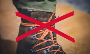 Czerwony krzyżyk na brązowym bucie trekkingowym z pomarańczowymi sznurówkami. Sznurowanie butów nie jest zalecane.