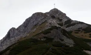 Grupa turystów wspina się po skalistej ścieżce na Giewont. Widoczny krzyż na szczycie. Trasa jest wymagająca.