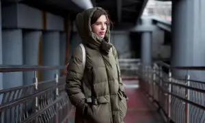 Kobieta w zielonej, pikowanej parkce z kapturem, stojąca na tle miejskiej architektury. Parka co to? To idealna ochrona przed zimnem.