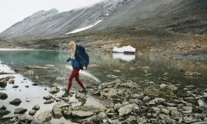Kobieta z plecakiem przemierza kamieniste wybrzeże jeziora. W tle góry, idealne dla skandynawskie marki outdoorowe.