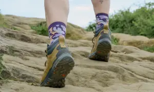 Wędrowiec stawia kroki po kamienistym szlaku, a jego **ciepłe stopy** w kolorowych skarpetkach i solidnych butach trekkingowych są gotowe na każdą przygodę.