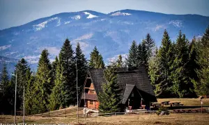 Drewniana bacówka PTTK na Krawcowym Wierchu, otoczona lasem świerkowym, z widokiem na ośnieżone góry.
