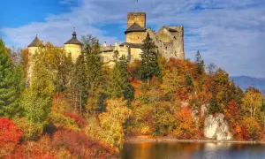 Zamek Dunajec w jesiennej szacie, otoczony kolorowymi drzewami, góruje nad spokojną taflą wody.