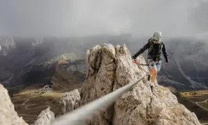 Kobieta na via ferrata, pokonująca skalną grań. Widok zapiera dech w piersiach, a droga jest wyzwaniem.