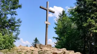 Drewniany krzyż na skalistym szczycie, punkt orientacyjny na łysica szlak. Otoczony zielenią drzew i błękitem nieba z chmurami.