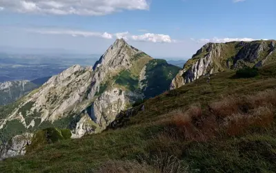 Widok na skaliste szczyty i zielone zbocza. Na pierwszym planie trawy, w oddali dolina małej łąki.