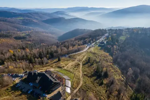 Widok z lotu ptaka na górski krajobraz jesienią. Widać hotel, parking, drogę i szlak równica z dzieckiem.