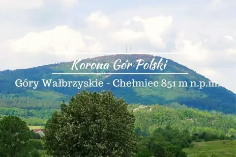Widok na górzysty krajobraz z dominującym szczytem Chełmiec. Na pierwszym planie bujna zieleń drzew, w tle łagodne zbocza Gór Wałbrzyskich.