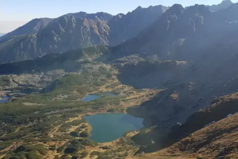 Widok na Tatry z licznymi stawami i kosodrzewiną. Szlak przez murowaniec prowadzi w kierunku górskich szczytów.