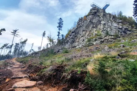 Kamienista ścieżka prowadzi ku skalnej grani z platformą widokową. To szlak na Trojak w Lądku-Zdroju, otoczony dziką przyrodą.