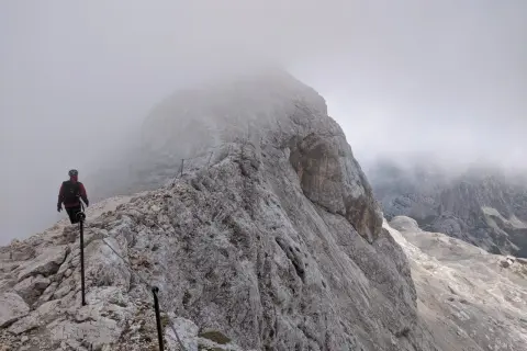 Turysta na skalistej ścieżce, wspinający się po via ferracie. Mgła otula szczyty, tworząc mistyczną atmosferę na szlakach Triglavu.