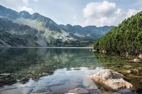 Dolina Pięciu Stawów z dzieckiem w tle, otoczona górami i lasem. Woda krystalicznie czysta, widać kamienie na dnie.