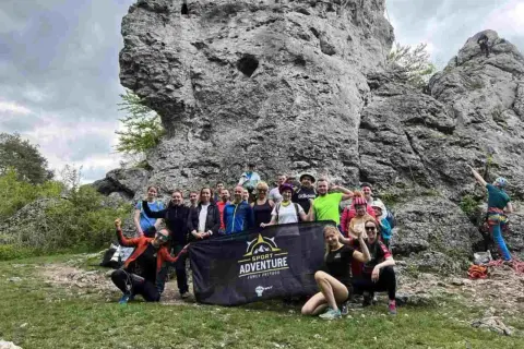 Grupa entuzjastów wspinaczki na Jurze Krakowsko-Częstochowskiej pozuje do zdjęcia z banerem "Sport Adventure".