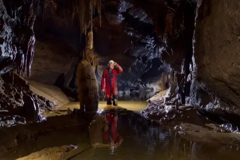 Eksplorator w czerwonym kombinezonie w jaskini z wodą. To jest właśnie speleologia co to – badanie podziemnych światów.
