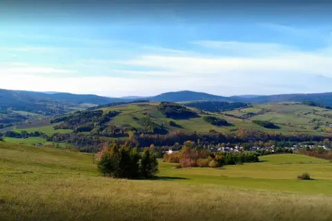 Malowniczy krajobraz z zielonymi wzgórzami i lasami, gdzieś w tle majaczy góra Grzywacka.