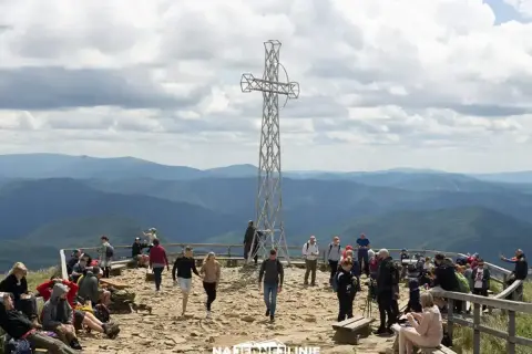 Tłum turystów na szczycie Tarnicy w Bieszczadach, podziwiających rozległą panoramę gór.