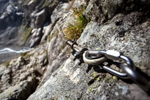 Stalowa lina i karabińczyk na skale, element ułatwiający wspinaczkę na via ferrata Czechy. Widok na zbocze.