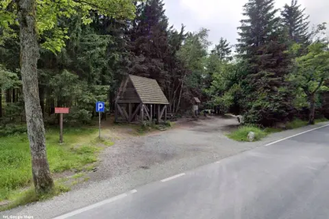 Drewniana wiata i parking przy leśnej drodze. To miejsce to Lisia Przełęcz, idealne na odpoczynek w otoczeniu drzew.
