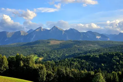 Widok na Tatry z przełęczy nad Łapszanką. Majestatyczne szczyty górskie na tle błękitnego nieba z chmurami.