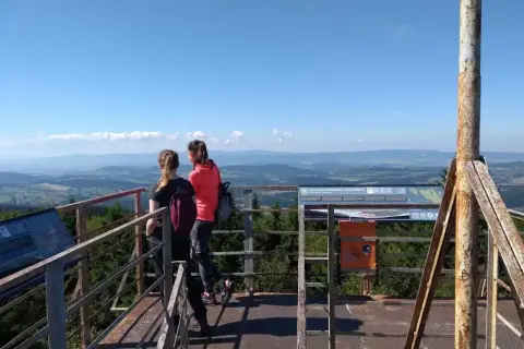 Dwie dziewczyny podziwiają panoramę z wieży widokowej na **kalenicy szczyt**. W tle rozciąga się malowniczy krajobraz Gór Sowich.