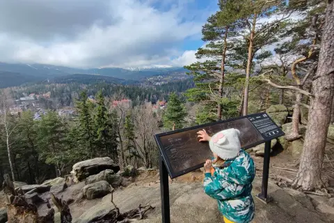 Dziecko w czapce z uszami poznaje mapę szlaków w Karpaczu. Widok na góry i miasto.