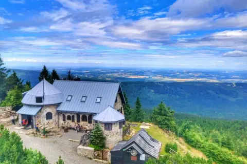 Kamienny schron turystyczny na szlaku w Górach Izerskich. Rozległa panorama krajobrazu z lasami i polami w oddali.