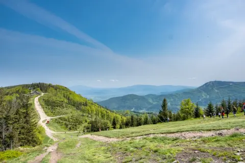 Widok na Beskid Śląski z trasą na Klimczok. W oddali widać szczyt z wieżą. Grupa turystów wędruje po zielonych zboczach.
