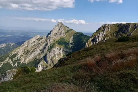 Widok na skaliste szczyty i zielone zbocza. Na pierwszym planie trawy, w oddali dolina małej łąki.