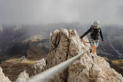 Kobieta na via ferrata, pokonująca skalną grań. Widok zapiera dech w piersiach, a droga jest wyzwaniem.