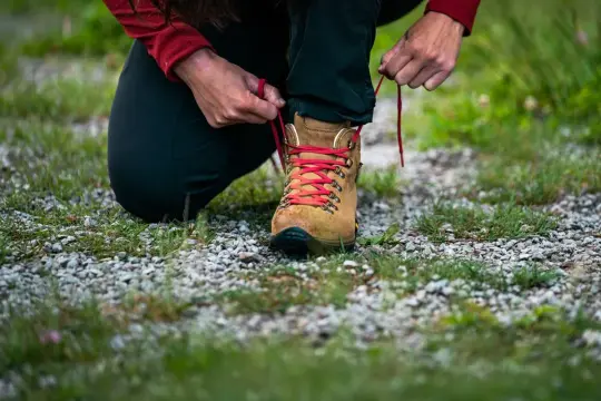 Długość wkładki a rozmiar buta – osoba sznuruje brązowy but trekkingowy z czerwonymi sznurówkami, przygotowując się do wędrówki.