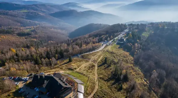 Widok z lotu ptaka na górski krajobraz jesienią. Widać hotel, parking, drogę i szlak równica z dzieckiem.