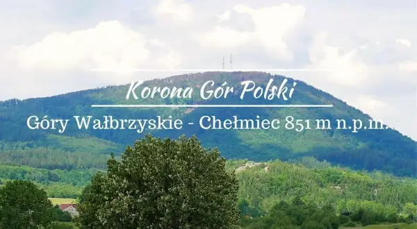 Widok na górzysty krajobraz z dominującym szczytem Chełmiec. Na pierwszym planie bujna zieleń drzew, w tle łagodne zbocza Gór Wałbrzyskich.
