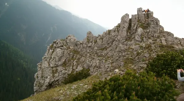 Sarnia skała wznosi się dumnie, otoczona zielenią. Na szczycie widać ludzi podziwiających panoramę.