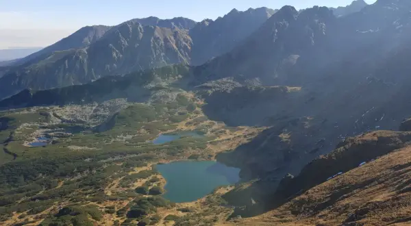 Widok na Tatry z licznymi stawami i kosodrzewiną. Szlak przez murowaniec prowadzi w kierunku górskich szczytów.