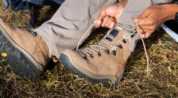 Przygotowanie do wędrówki. Osoba sznuruje brązowe buty trekkingowe z podeszwą Vibram XS Trek, gotowa na przygodę.