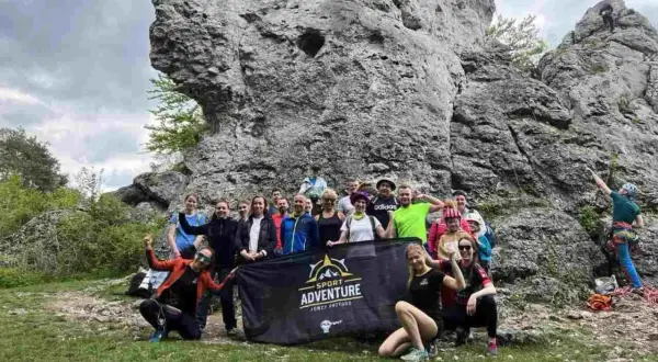Grupa entuzjastów wspinaczki na Jurze Krakowsko-Częstochowskiej pozuje do zdjęcia z banerem "Sport Adventure".